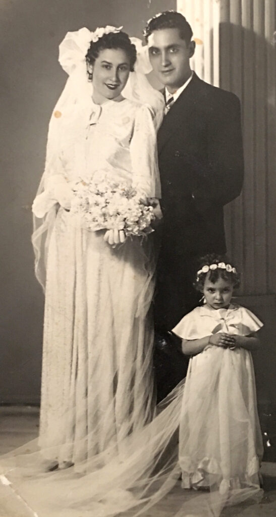 Bride in long dress with long sleeves and bouquet; groom in suit; little girl in white dress and headband