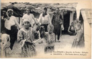 A historic postcard labeled “Salonica — The Vardar district, Refugees,” showing adults and children gathered outside temporary structures.