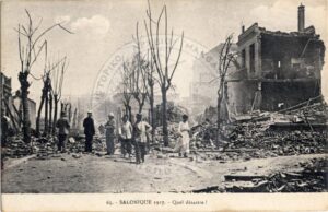 Historic postcard labeled “Salonique 1917 — Quel désastre!” showing fire-damaged buildings, leafless trees, and people gathered in a rubble-strewn street.