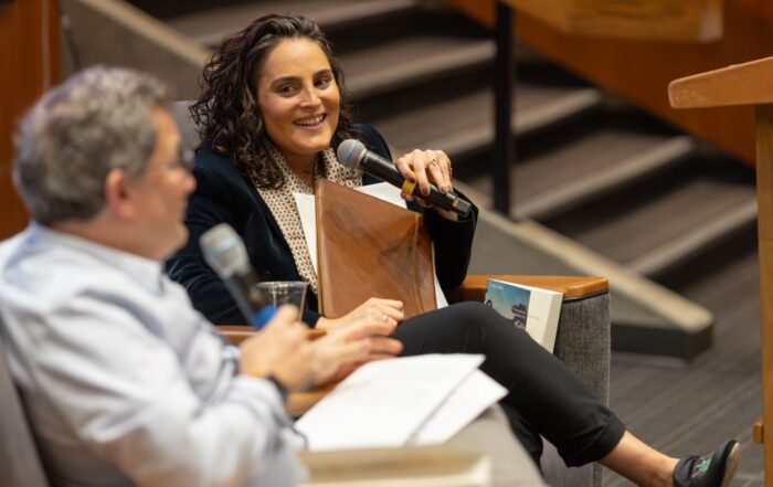 Gilah Kletenik smiles while speaking into a microphone during a seated conversation.