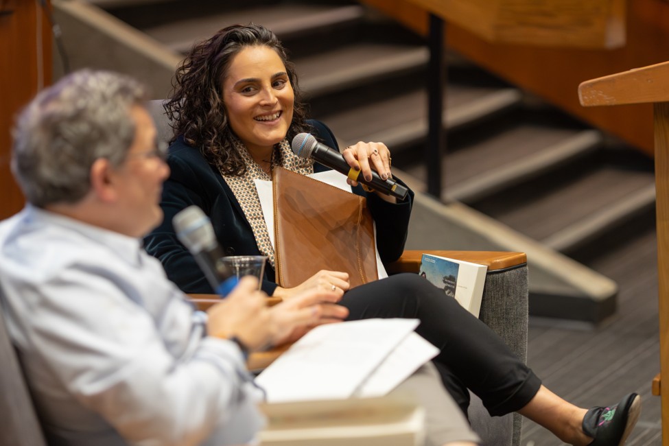 Gilah Kletenik smiles while speaking into a microphone during a seated conversation.