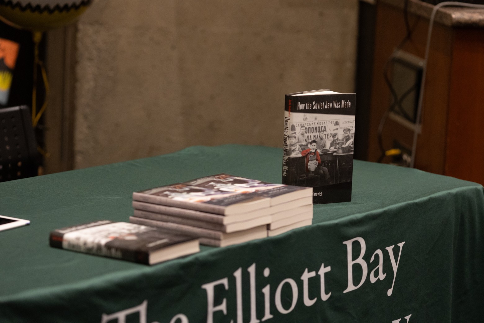Stacks of books sit on a green-covered table, with one copy of How the Soviet Jew Was Made standing upright.